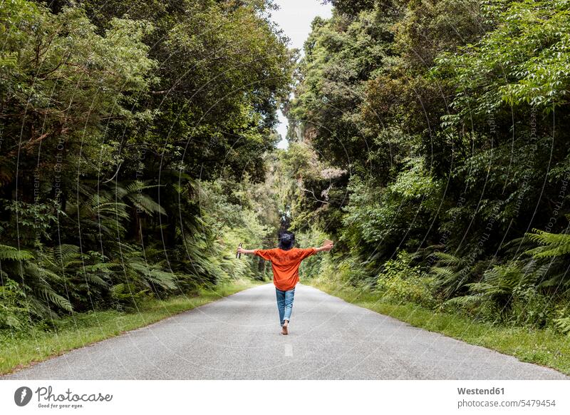 Young man walking with arms outstretched on country road in forest color image colour image outdoors location shots outdoor shot outdoor shots day daylight shot