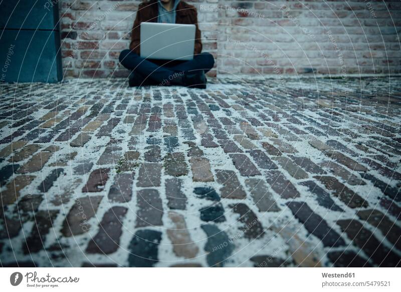 Teenager using laptop and sitting on a stone floor in the city criminals computers Laptop Computer Laptop Computers laptops notebook Seated in the evening