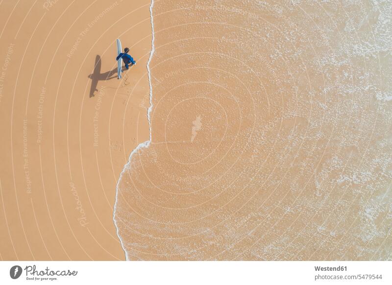Portugal, Algarve, Sagres, Praia da Mareta, aerial view of man carrying surfboard on the beach sand sandy drone drones water alone solitary water's edge
