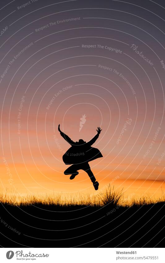 Carefree man wearing jacket jumping with arms outstretched against sky during sunset color image colour image outdoors location shots outdoor shot outdoor shots