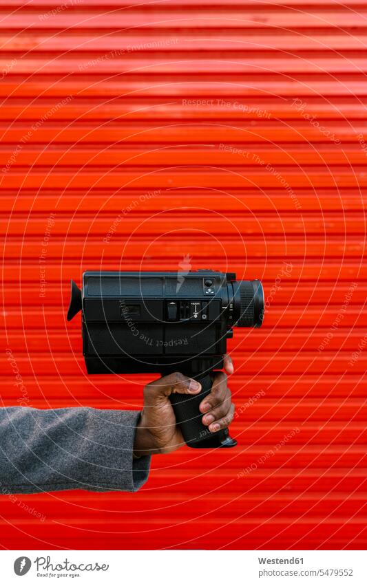 Man holding 80's film camera against red wall color image colour image outdoors location shots outdoor shot outdoor shots day daylight shot daylight shots