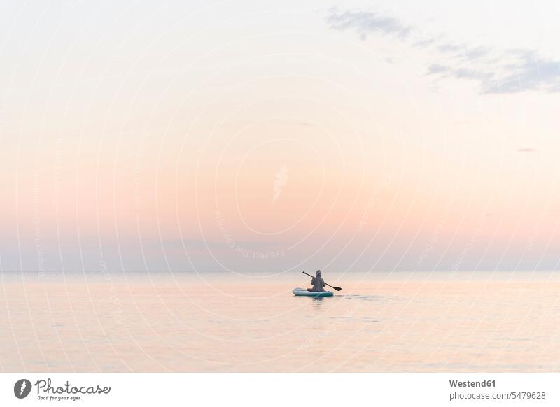 Boy with oar paddleboarding on sea during sunset color image colour image outdoors location shots outdoor shot outdoor shots sunsets sundown atmosphere Idyllic