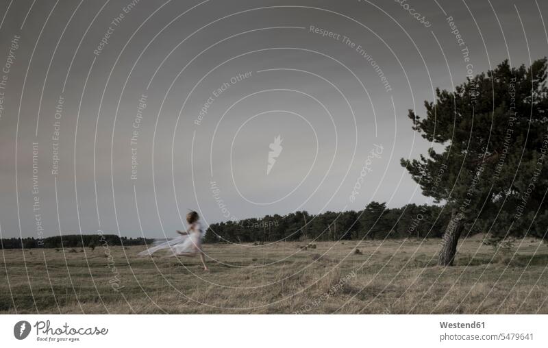 Germany, Bavaria, Froettmaning Heath, young woman wearing a tulle dress and running fashion fashionable on the move on the go fairy tale fairy tales white