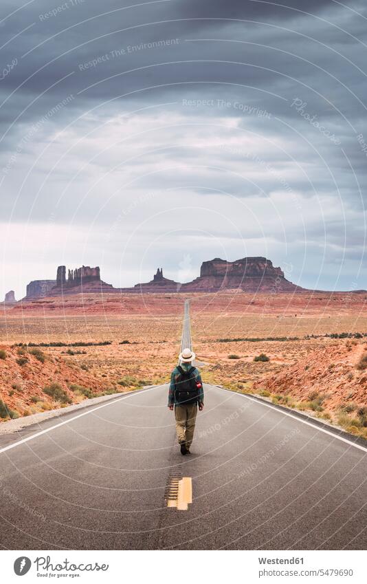 USA, Utah, Man with backpack walking on road to Monument Valley rucksacks backpacks back-packs young man young men streets roads standing going males Adults