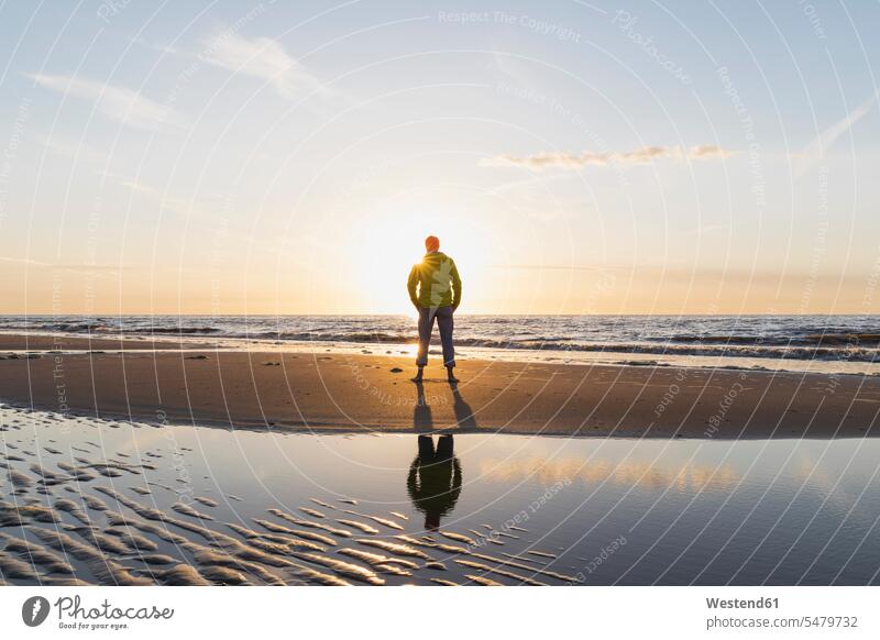 Full length of senior man standing on shore at beach during sunset, North Sea Coast, Flanders, Belgium color image colour image outdoors location shots