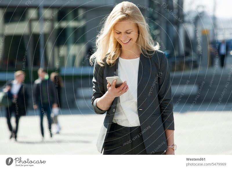 Portrait of smiling blond businesswoman looking at cell phone businesswomen business woman business women Smartphone iPhone Smartphones business people