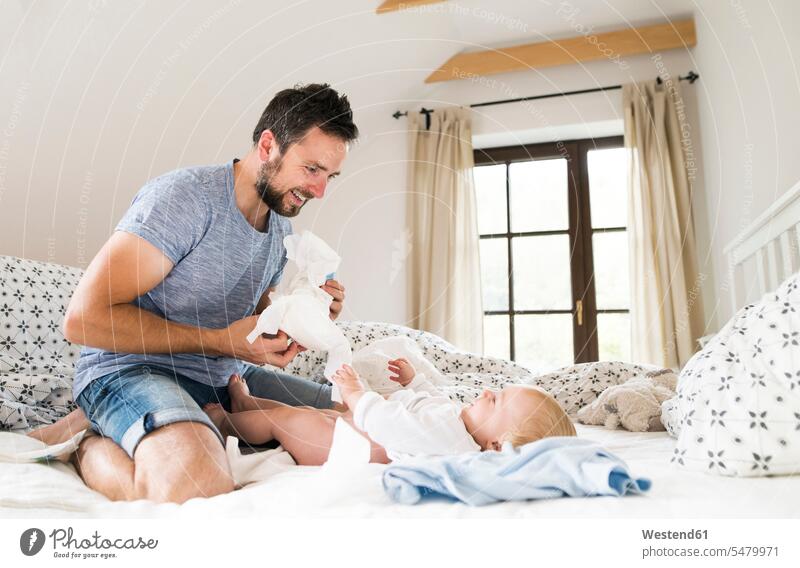 Father changing baby's diapers on bed babies infants change Nappy father pa fathers daddy dads papa people persons human being humans human beings parents