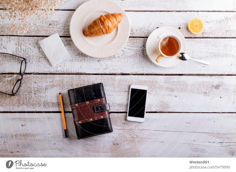 Table with croissant, tea, smart phone and personal organiser Tea Teas Drink beverages Drinks Beverage food and drink Nutrition Alimentation Food and Drinks