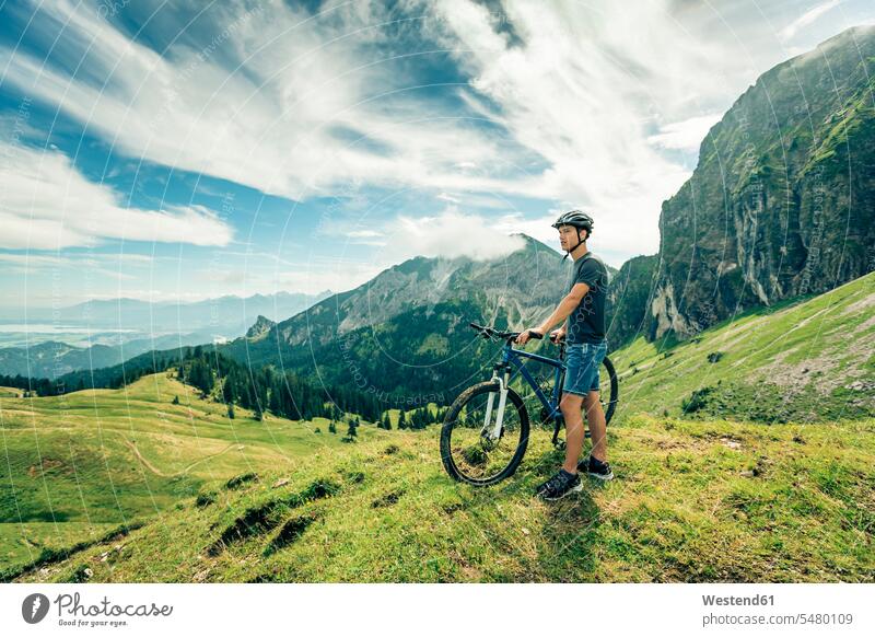 Germany, Bavaria, Pfronten, young man with mountain bike on alpine meadow near Aggenstein View Vista Look-Out outlook men males standing Adults grown-ups