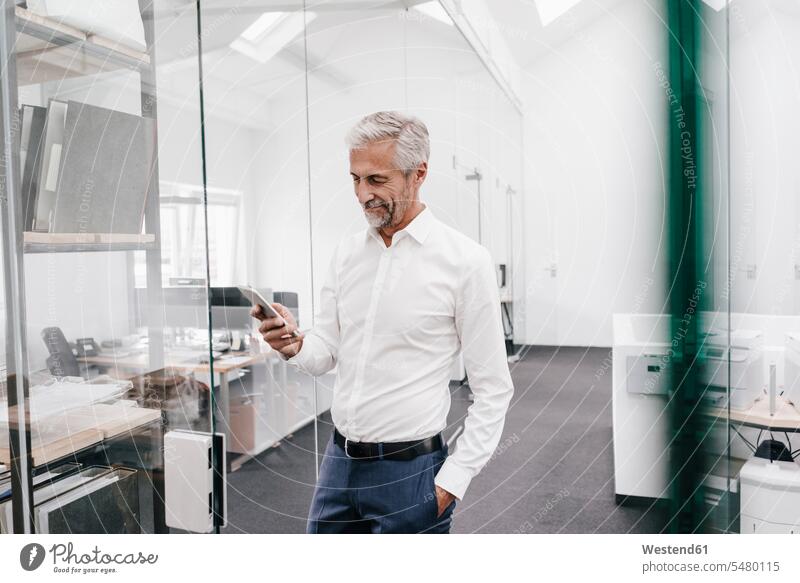 Mature businessman holding cell phone in office Businessman Business man Businessmen Business men mobile phone mobiles mobile phones Cellphone cell phones