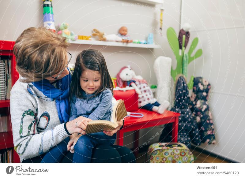 Senior woman with granddaughter on her lap reading out a book caucasian caucasian ethnicity caucasian appearance european looking down indoors indoor shot
