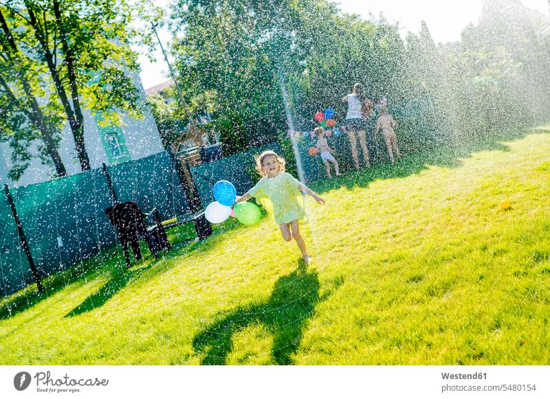 Little girl having fun with lawn sprinkler in the garden females girls child children kid kids people persons human being humans human beings playing running
