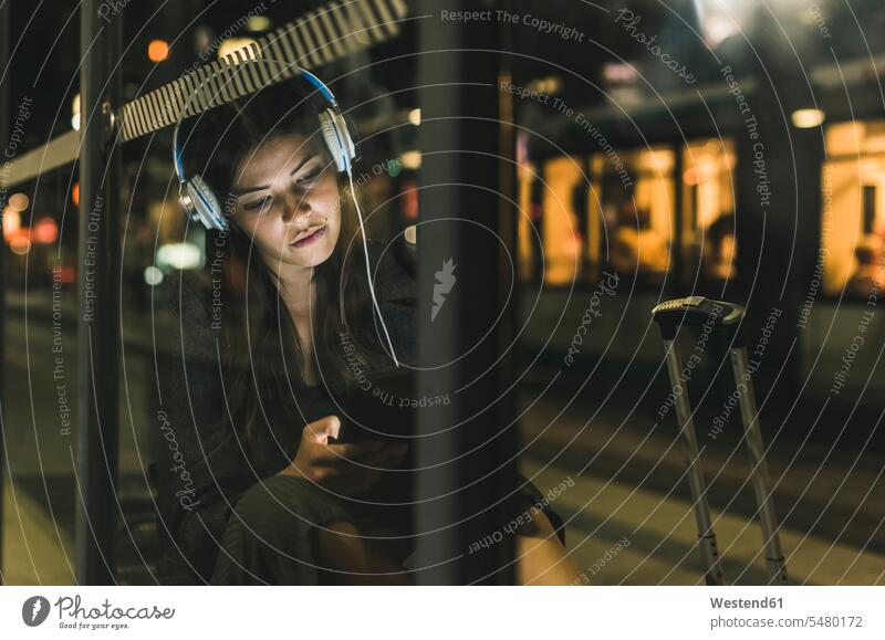 Portrait of young woman with headphones waiting at the station by night using tablet at night nite night photography females women headset Adults grown-ups