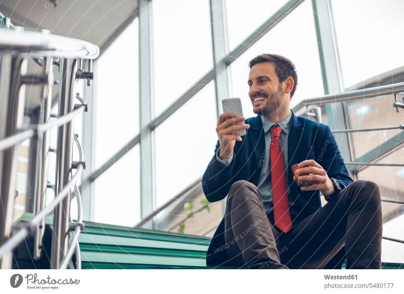 Smiling businessmann sitting on stairs using cell phone Businessman Business man Businessmen Business men Smartphone iPhone Smartphones business people