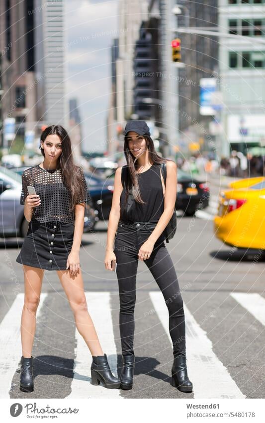 USA, New York City, two fashionable twin sisters standing on zebra crossing in Manhattan female friends Fun having fun funny New York State siblings
