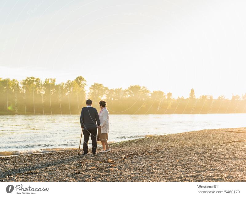 Senior couple standing on at riverside by sunset senior couple elder couples senior couples adult couple adult couples twosomes partnership people persons