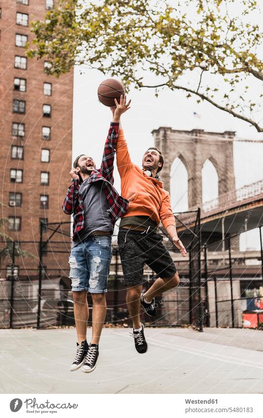 USA, New York, two young men playing basketball on an outdoor court man males jumping Leaping basketballs friends Adults grown-ups grownups adult people persons