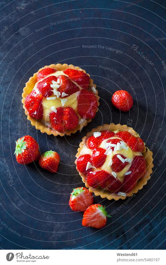 Two strawberry tartlets with custard and white chocolate shaving on dark ground red garnished ready to eat ready-to-eat short crust short pastry