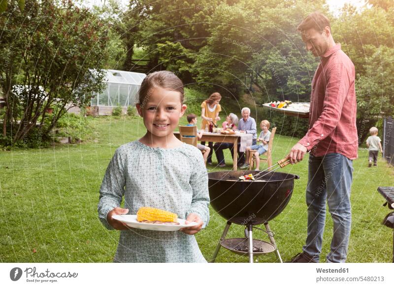 Smiling girl holding plate with corn cob on a family barbecue barbecueing Barbecuing grilling garden gardens domestic garden smiling smile Barbecue BBQ Barbeque