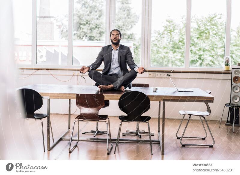 Young businessman sitting cross-legged on desk in office tailor seat place of work work place office room office rooms offices business life business world