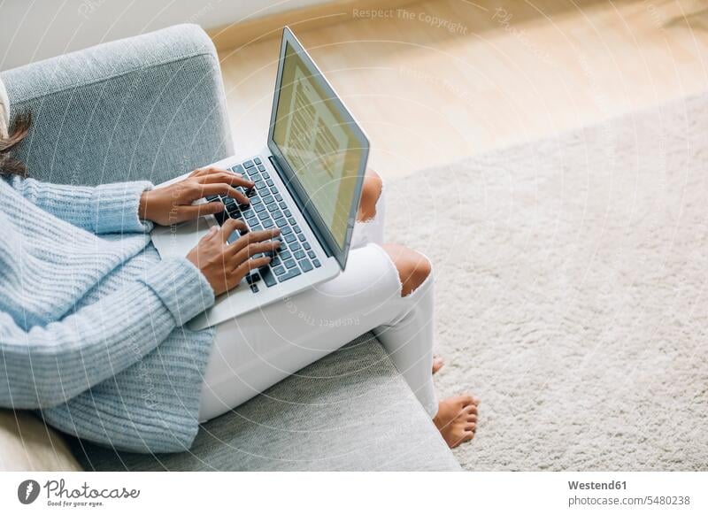 Young woman sitting on couch at home using laptop, partial view Laptop Computers laptops notebook females women computer computers Adults grown-ups grownups