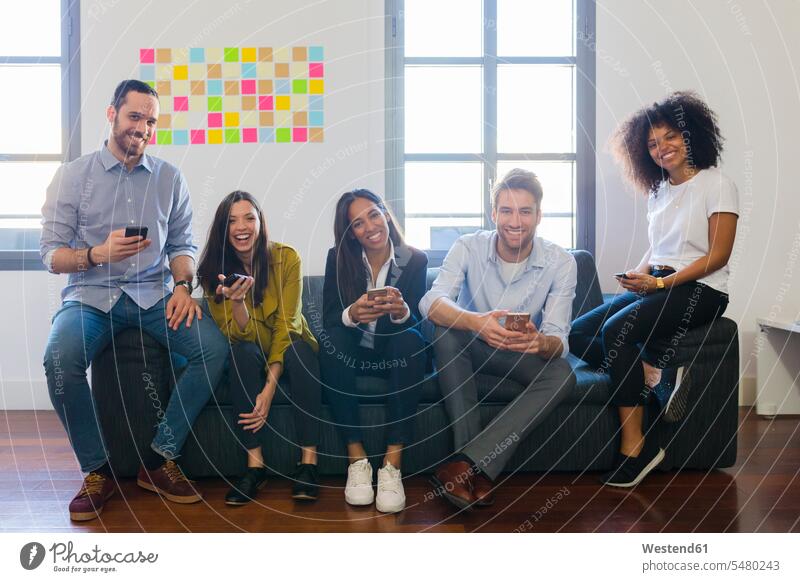 Portrait of happy colleagues sitting on couch with cell phones office offices office room office rooms workplace work place place of work mobile phone mobiles