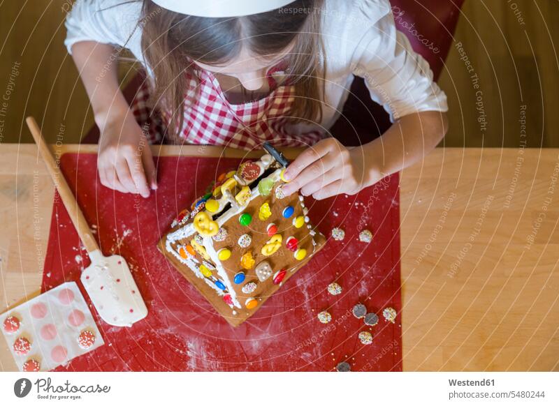 Girl garnishing gingerbread house, top view girl females girls Gingerbread house Gingerbread Houses child children kid kids people persons human being humans