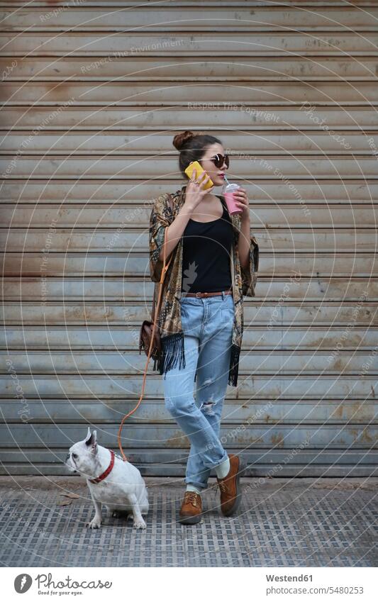 Young woman drinking smoothie and telephoning with smartphone while waiting with her dog on the street Spain bun beauty beautiful accessibility accessible