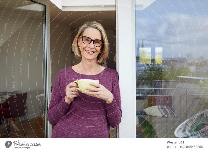 Portrait of smiling mature woman holding coffee mug on balcony smile Coffee portrait portraits window windows females women Drink beverages Drinks Beverage