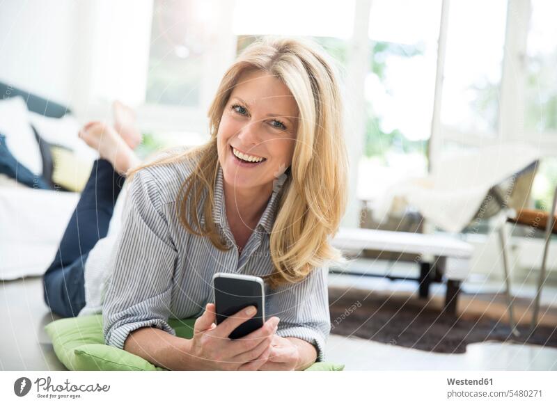 Mature woman lying on floor, using smartphone living room living rooms livingroom blond blond hair blonde hair Smartphone iPhone Smartphones mobile phone