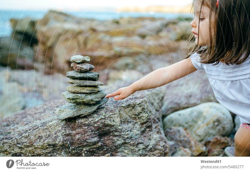 Girl with stack of stones at rocky coast girl females girls cairn rocks child children kid kids people persons human being humans human beings stacked stacks