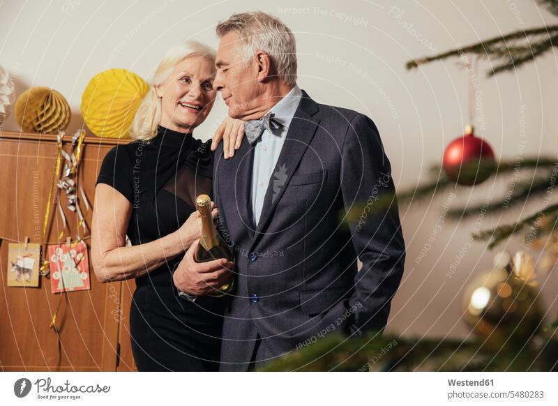 Senior couple holding bottle of Champagne on New Yera's Eve Germany active seniors well-dressed dressed up toothy smile big smile open smile laughing