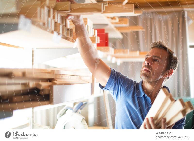 Man taking wooden frame from shelf in canvas workshop man men males carpenter carpenters cabinetmakers working At Work take Adults grown-ups grownups adult