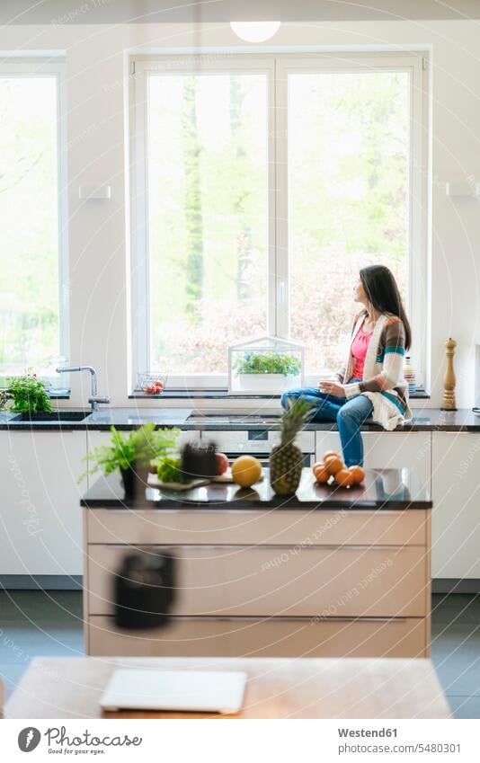 Woman in kitchen looking out of window relaxed relaxation serious earnest Seriousness austere woman females women sitting Seated relaxing Adults grown-ups