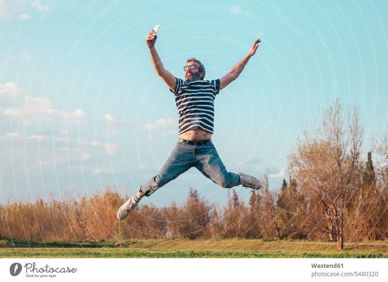 Man jumping in the air while taking photo with smartphone man men males Selfie Selfies Leaping Adults grown-ups grownups adult people persons human being humans