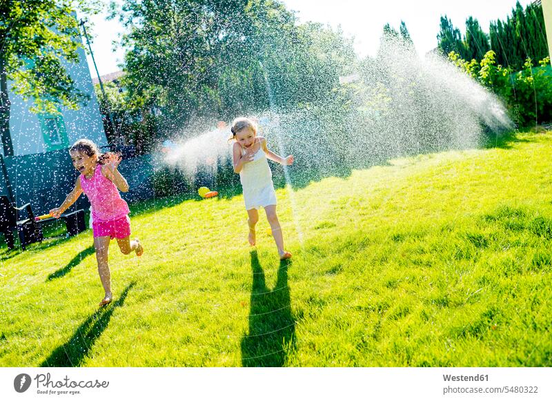 Children having fun with lawn sprinkler in the garden water girl females girls child children kid kids people persons human being humans human beings playing