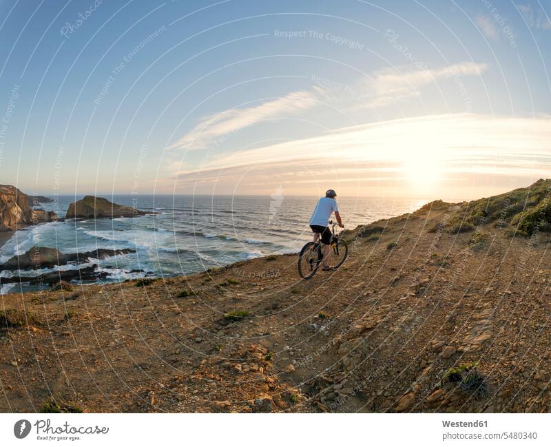 Portugal, Senior man mountain biking at the sea tourist tourists beach beaches men males bicycle bikes bicycles sunset sunsets sundown riding senior men