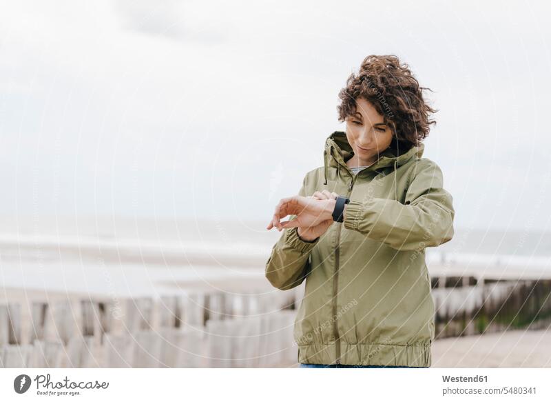Woman on the beach looking at her smartwatch woman females women smart watch beaches Adults grown-ups grownups adult people persons human being humans