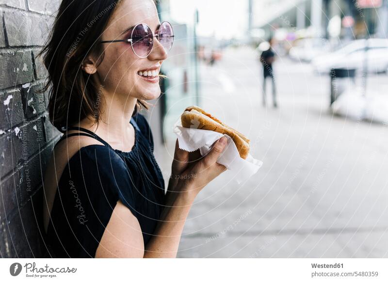 Smiling woman with Hot Dog leaning against wall hot dog Hotdog Hot-Dogs hot dogs Hotdogs females women Adults grown-ups grownups adult people persons