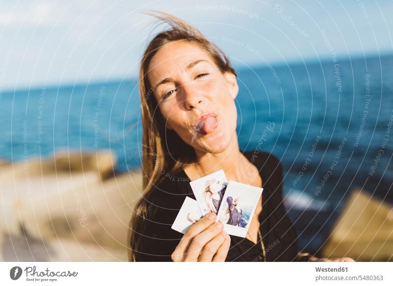 Cheeky young woman showing instant photos of herself at the seafront photograph photographs Showing happiness happy females women image images picture pictures