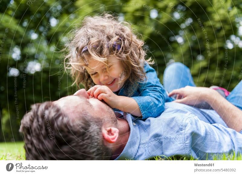 Father cuddling with daughter on meadow in park father fathers daddy dads papa lying laying down lie lying down daughters parents family families people persons