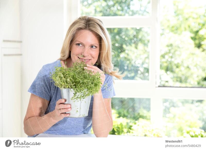 Portrait of smiling woman with pot of herbs in the kitchen culinary herb culinary herbs kitchen herb smelling females women spice flavouring flavoring spices