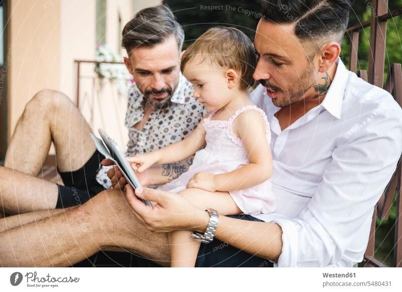 Gay couple with daughter on balcony using digital tablet twosomes partnership couples daughters digitizer Tablet Computer Tablet PC Tablet Computers iPad