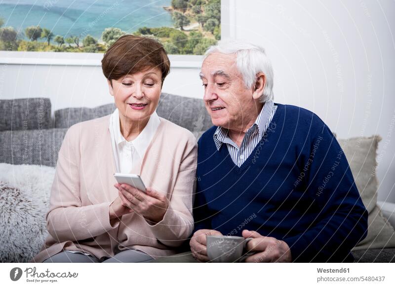 Senior couple lying on couch using smartphone on the phone call telephoning On The Telephone calling Smartphone iPhone Smartphones message reading