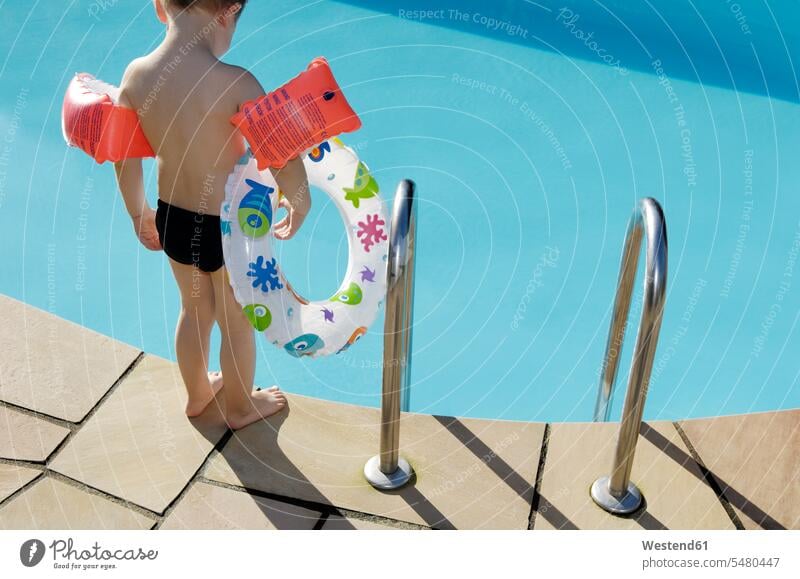 Back view of little boy with floating tire and water wings standing at pool edge caucasian caucasian ethnicity caucasian appearance european barefoot naked feet