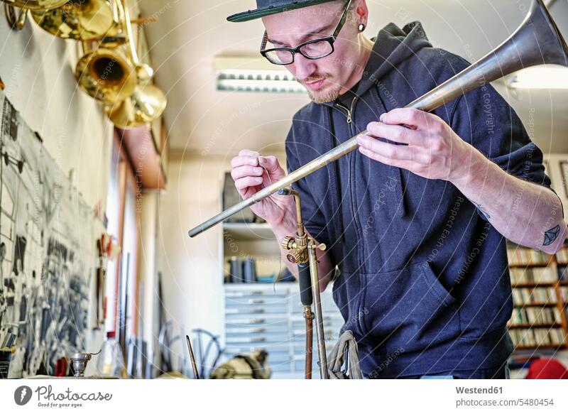 Instrument maker making trumpet in workshop instrument maker man males building Craftsperson Craftspersons Craftspeople working At Work trumpets craftsman trade
