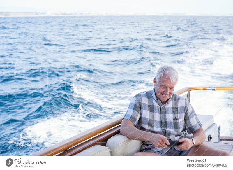 Senior man on a boat trip looking at cell phone mobile phone mobiles mobile phones Cellphone cell phones sitting Seated smiling smile men males boats telephones
