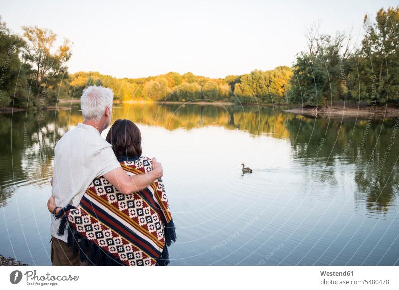 Senior couple at a lake looking at duck senior men senior man elder man elder men senior citizen embracing embrace Embracement hug hugging lakes twosomes