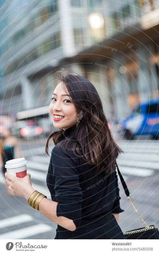 USA, New York City, Manhattan, portrait of smiling young woman with coffee to go crossing the street females women Coffee to Go takeaway coffee portraits Adults