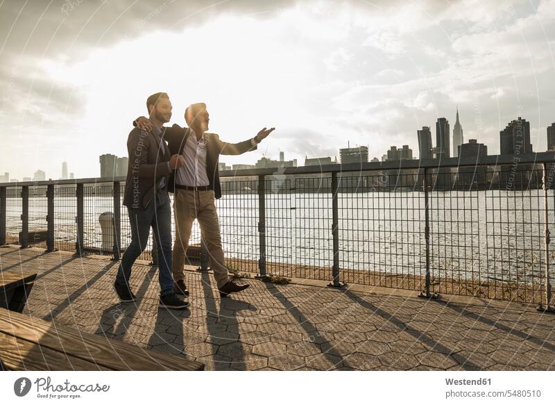 USA, New York City, two businessmen walking together along East River New York State Businessman Business man Businessmen Business men males going United States